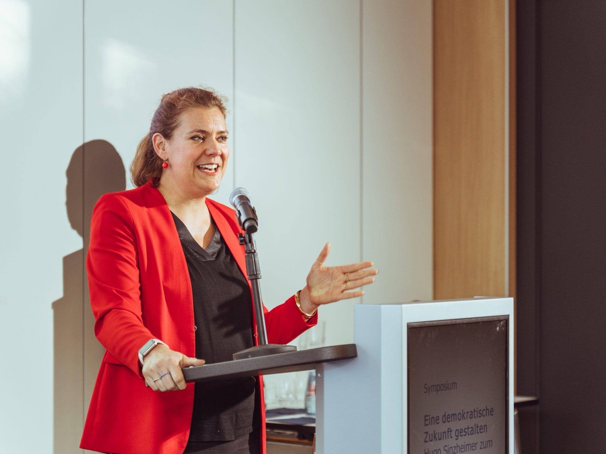 - Europäische Akademie der Arbeit Prof. Dr. Johanna Wenckebach in rotem Blazer spricht an einem Rednerpult während der Keynote zu Ehren von Hugo Sinzheimer.