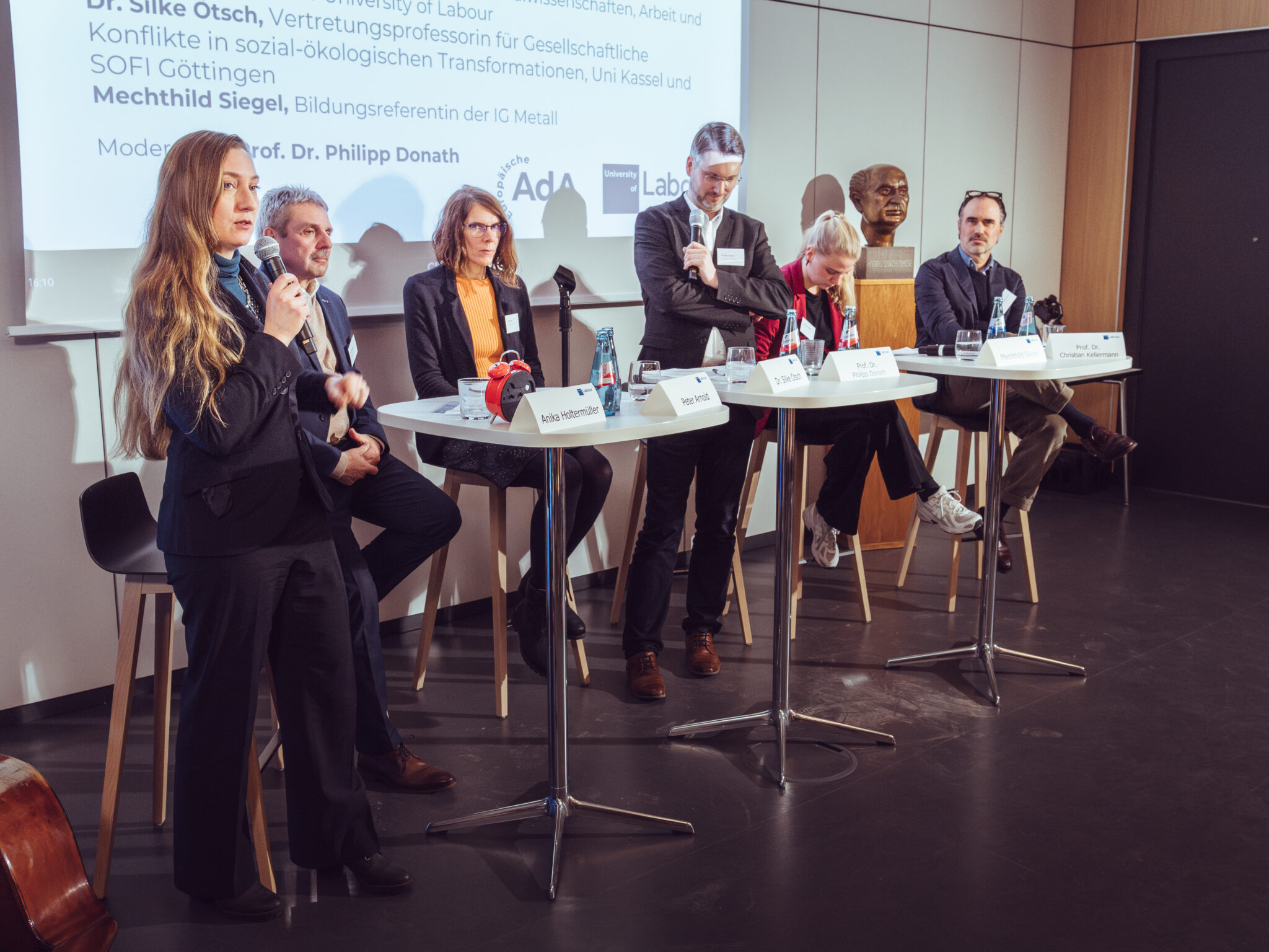 - Europäische Akademie der Arbeit Podiumsdiskussion mit fünf Personen, die über Mitbestimmung in der digitalen Transformation sprechen, im Hintergrund ein...